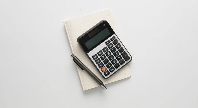 Calculator and pen placed on a notebook on a clean white surface.