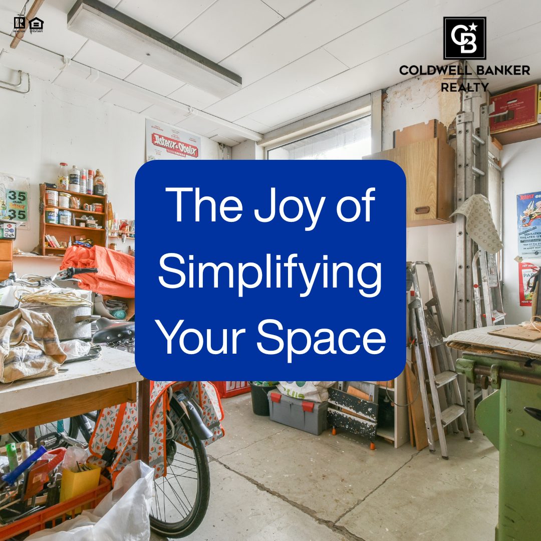 A cluttered garage filled with tools, shelves, bikes, and household items, with a bold blue text overlay reading “The Joy of Simplifying Your Space,” alongside the Coldwell Banker Realty logo.